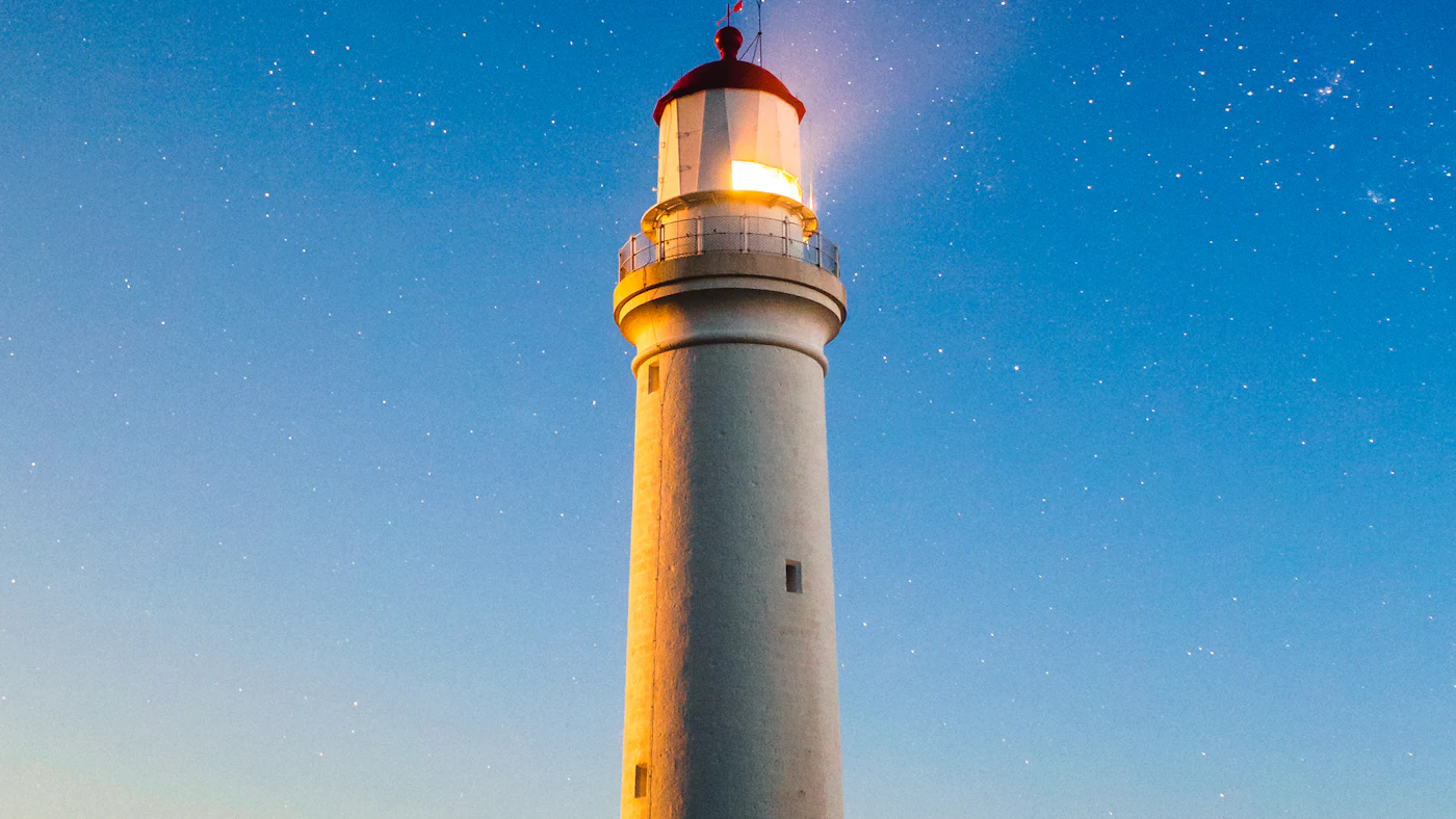 A white lighthouse lit at dusk under a starry sky